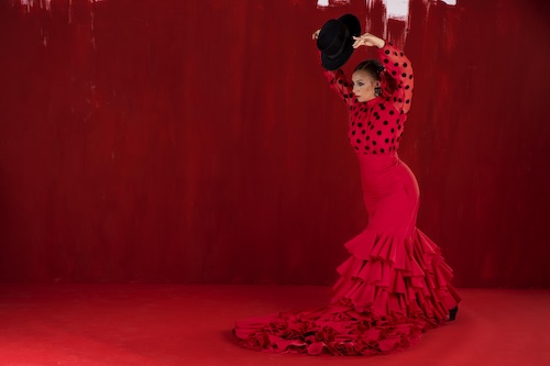 Flamenco dancer on a red stage dressed in red with a black hat.